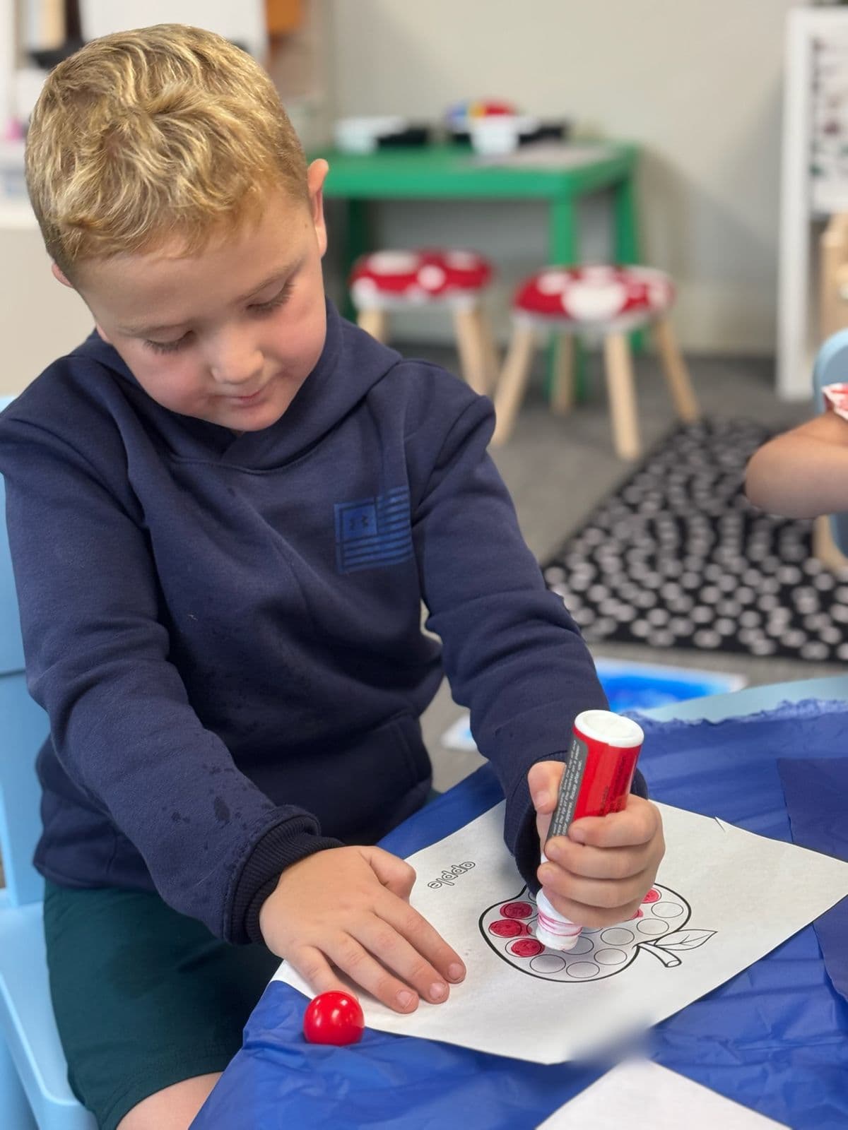 A boy fills in an apple worksheet with a red dot marker.