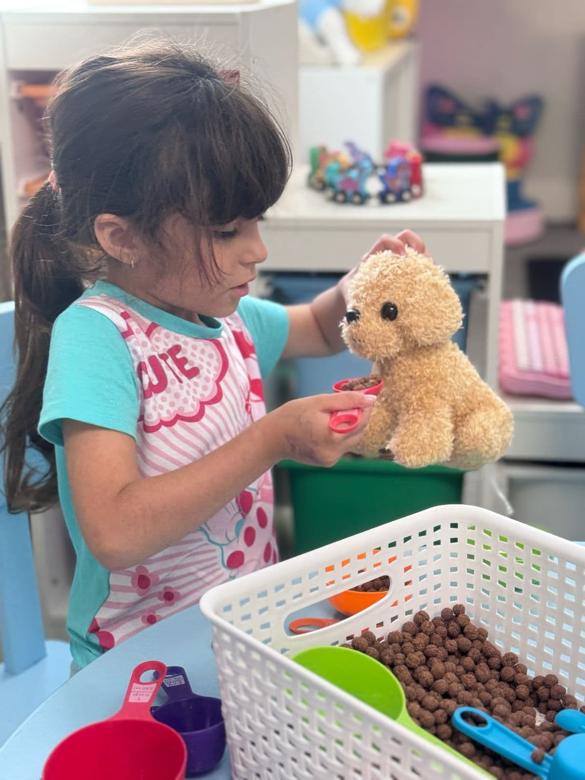 A preschooler holds a measuring cup of cereal up to a toy puppy.