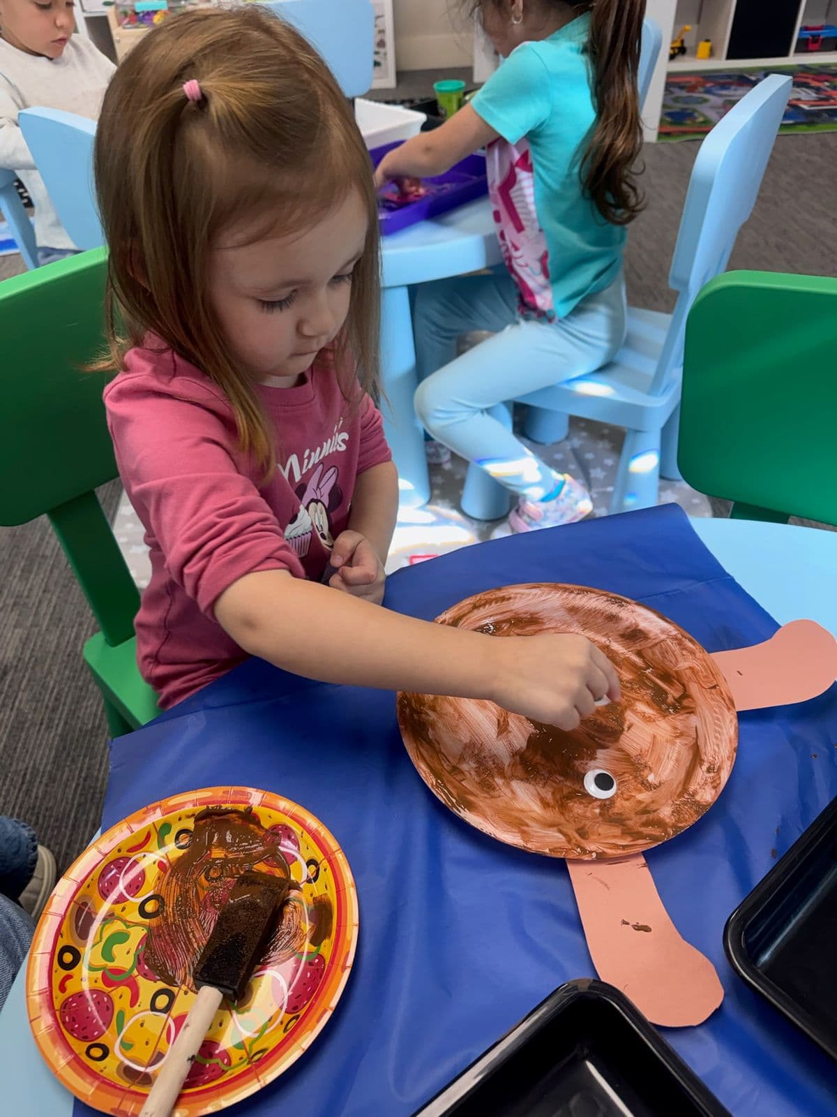 A preschooler adds a googly eye to a brown-painted paper-plate turtle.