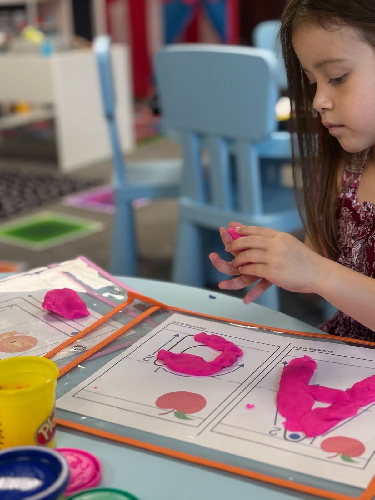 A preschooler presses pink play dough into letter shapes on a tracing mat.