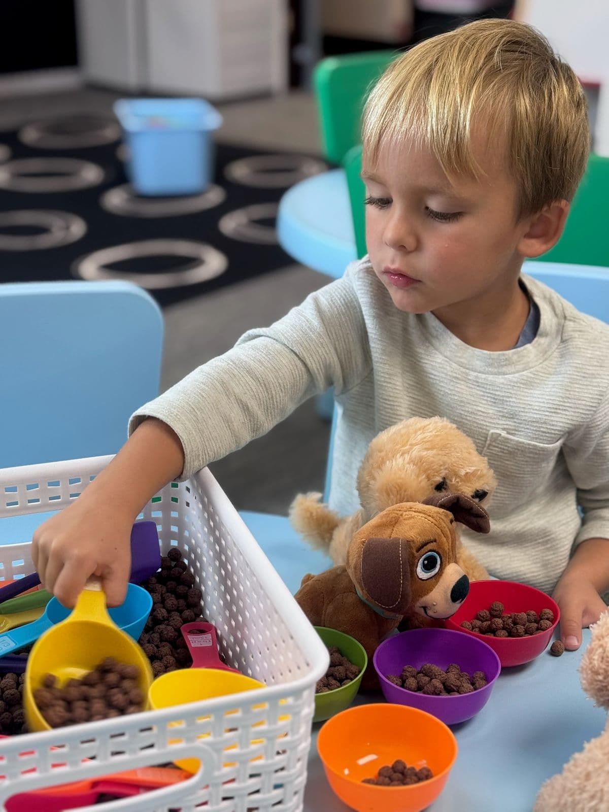 A boy scoops cereal into colorful bowls to feed a row of toy puppies.