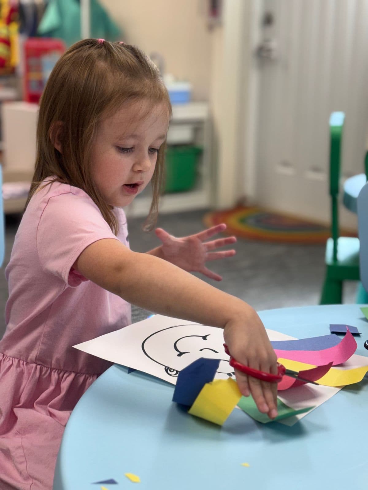 A preschooler cuts colorful paper strips for a rainbow art project.