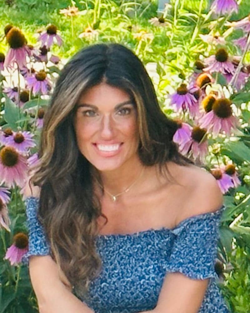 Portrait of Nicole Disa, founder and director of Little Ivy, smiling in a garden of coneflowers.