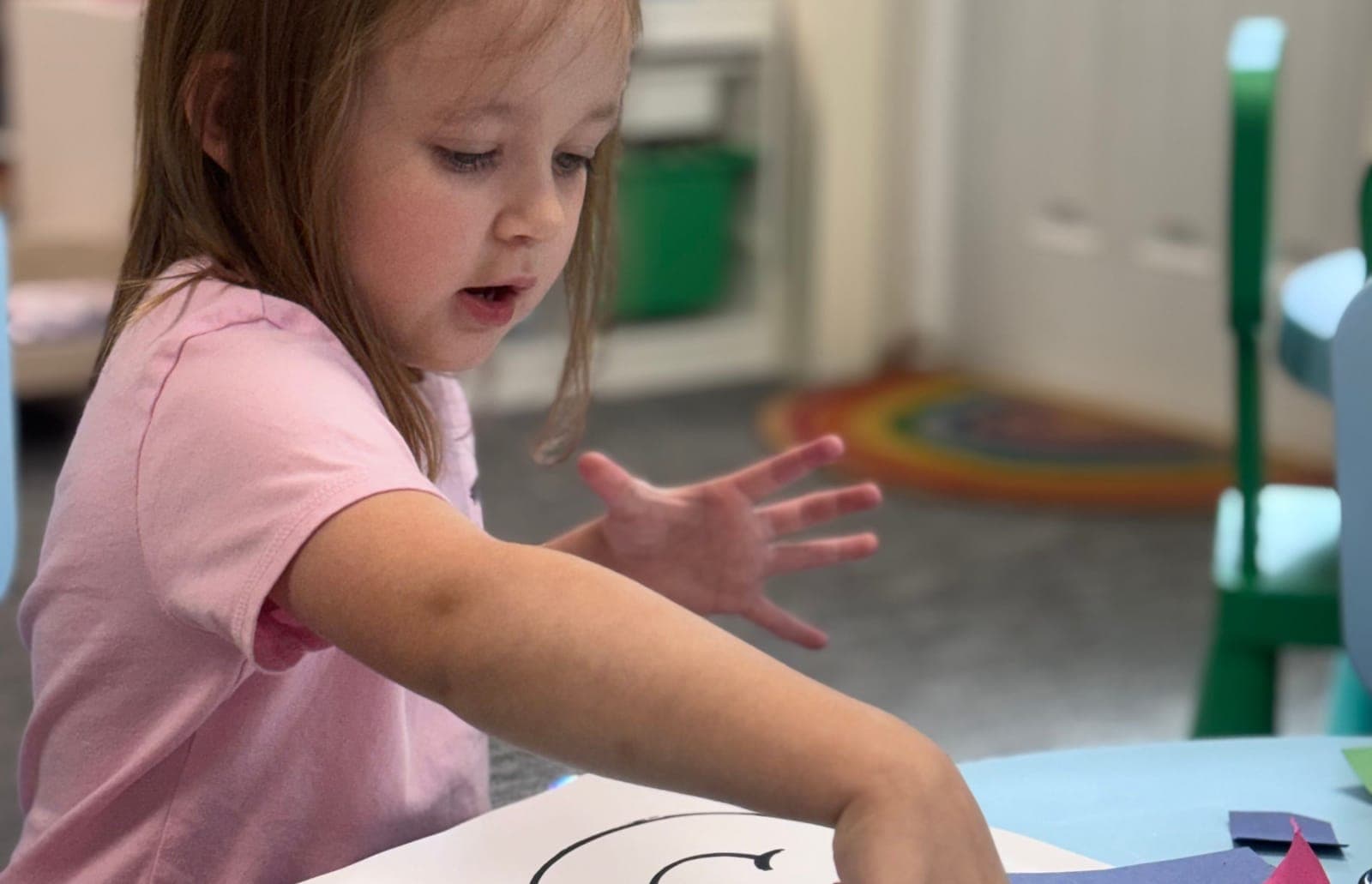 A preschooler concentrating on a paper-cutting project at a Little Ivy classroom table.