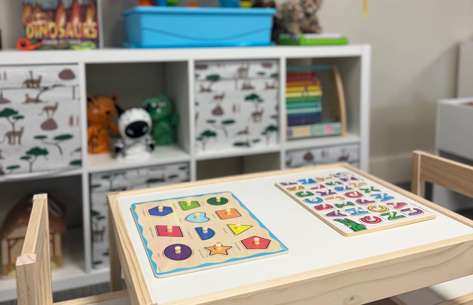 Wooden shape and alphabet puzzles set out on a child-size table in a Little Ivy classroom.